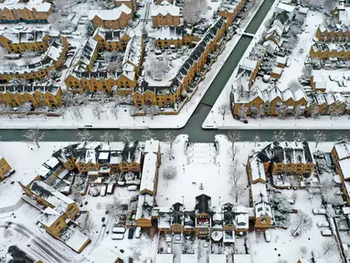 Pemandangan udara menunjukkan salju menutupi atap rumah dan jalan, mengelilingi kanal di Wapping, London timur, Senin (10/12/2022). Salju dan es telah menyapu sebagian Inggris, dengan suhu dingin dan kabut yang membekukan serta salju diperkirakan akan tetap ada sepanjang minggu ini. (Photo by Daniel LEAL / AFP)