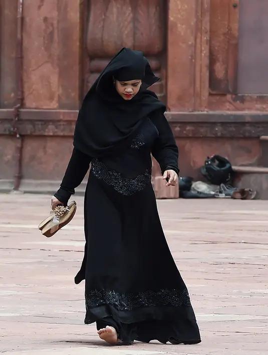 Seorang wanita membawa sandal berjalan di masjid Jama  di kawasan lama New Delhi, India (30/7/2019). Masjid ini didirikan oleh Kaisar Mogul, Syah Jehan, yang juga membangun Taj Mahal. (AFP Photo/Money Sharma)