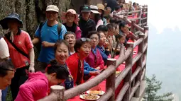 Wisatawan menyantap makanan pada acara perjamuan di sepanjang tepi tebing di Laojun Mountain provinsi Henan, China. Wisatawan menikmati berbagai suguhan makanan di jalanan selebar enam kaki yang menempel pada tebing setinggi 2.000 meter. (AFP)