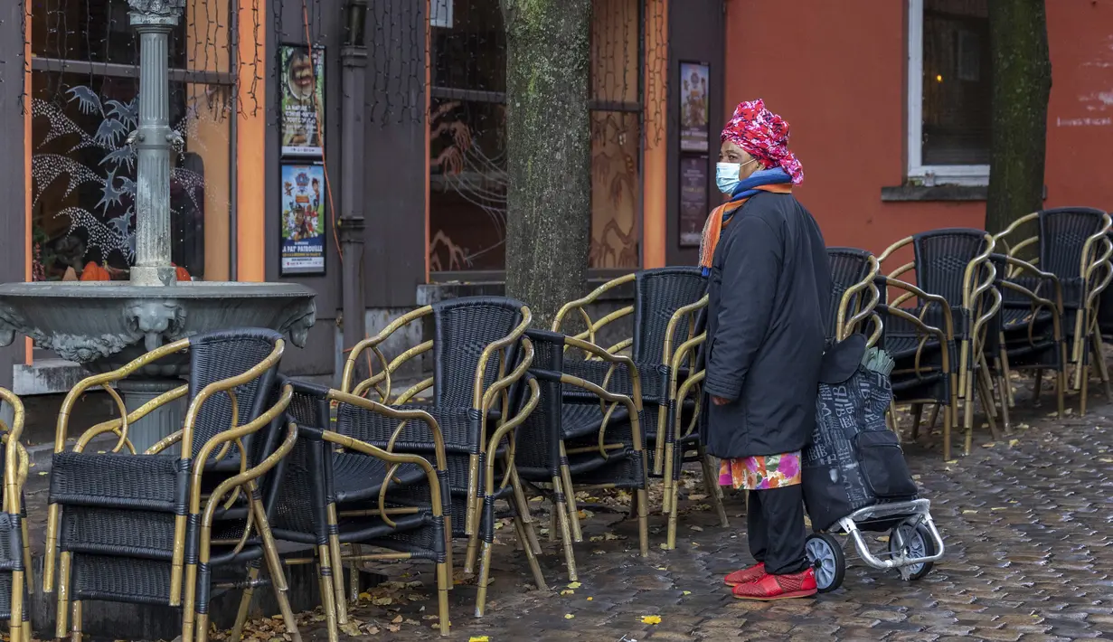 Seorang wanita mengenakan masker saat melewati teras kosong di kawasan Marrolles di Brussels, Rabu (17/11/2021). Pemerintah Belgia mewajibkan kembali penggunaan masker dan memberlakukan warga bekerja dari rumah dalam upaya untuk menahan lonjakan baru kasus COVID-19. (AP Photo/Olivier Matthys)