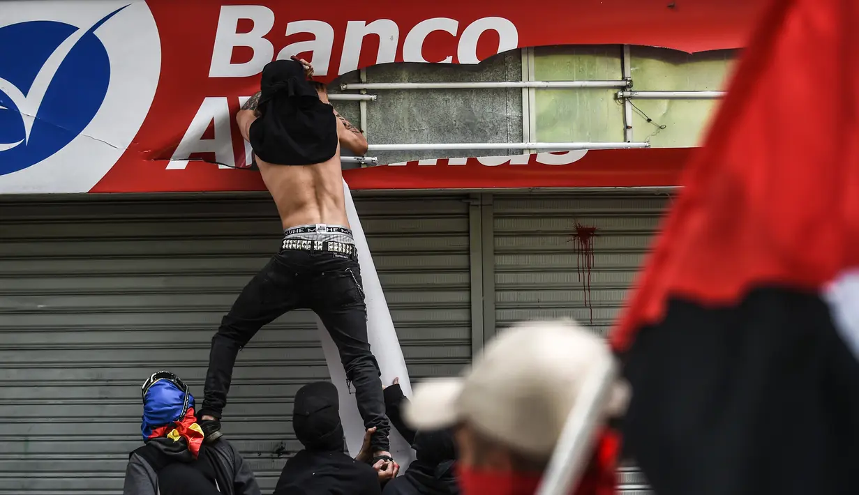 Seorang demonstran melakukan pengrusakan saat saat peringatan Hari Buruh di Medellin, Kolombia (1/5). Hari Buruh lahir dari berbagai rentetan perjuangan kelas pekerja untuk meraih kendali ekonomi-politis hak-hak industrial. (AFP/Joaquin Sarmiento)