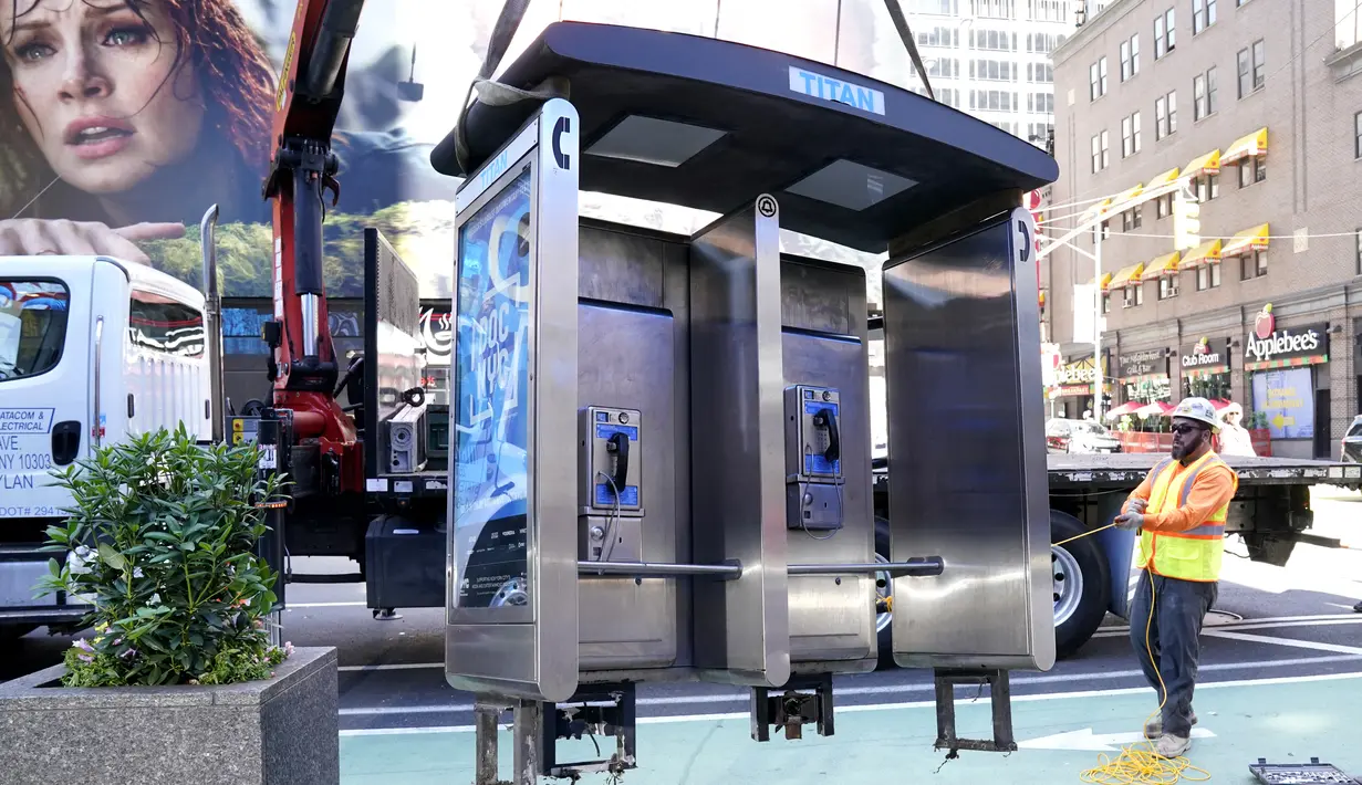 Para pekerja memindahkan bilik telepon umum terakhir NYC di dekat Seventh Avenue dan 50th Street di Midtown Manhattan, New York City, pada 23 Mei 2022. Telepon umum mulai menghilang dari jalan-jalan di New York pada awal 2000-an saat penggunaan telepon selular menyebar, dan kemudian menghilang lebih cepat pada 2010-an saat terjadi booming telepon pintar. (TIMOTHY A. CLARY / AFP)