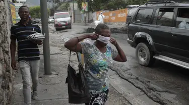 Seorang wanita berjalan melewati pihak berwenang setempat yang memindahkan jenazah pria yang dibakar massa di Port-au-Prince, Haiti, Selasa (25/4/2023). (AP Photo/Odelyn Joseph)