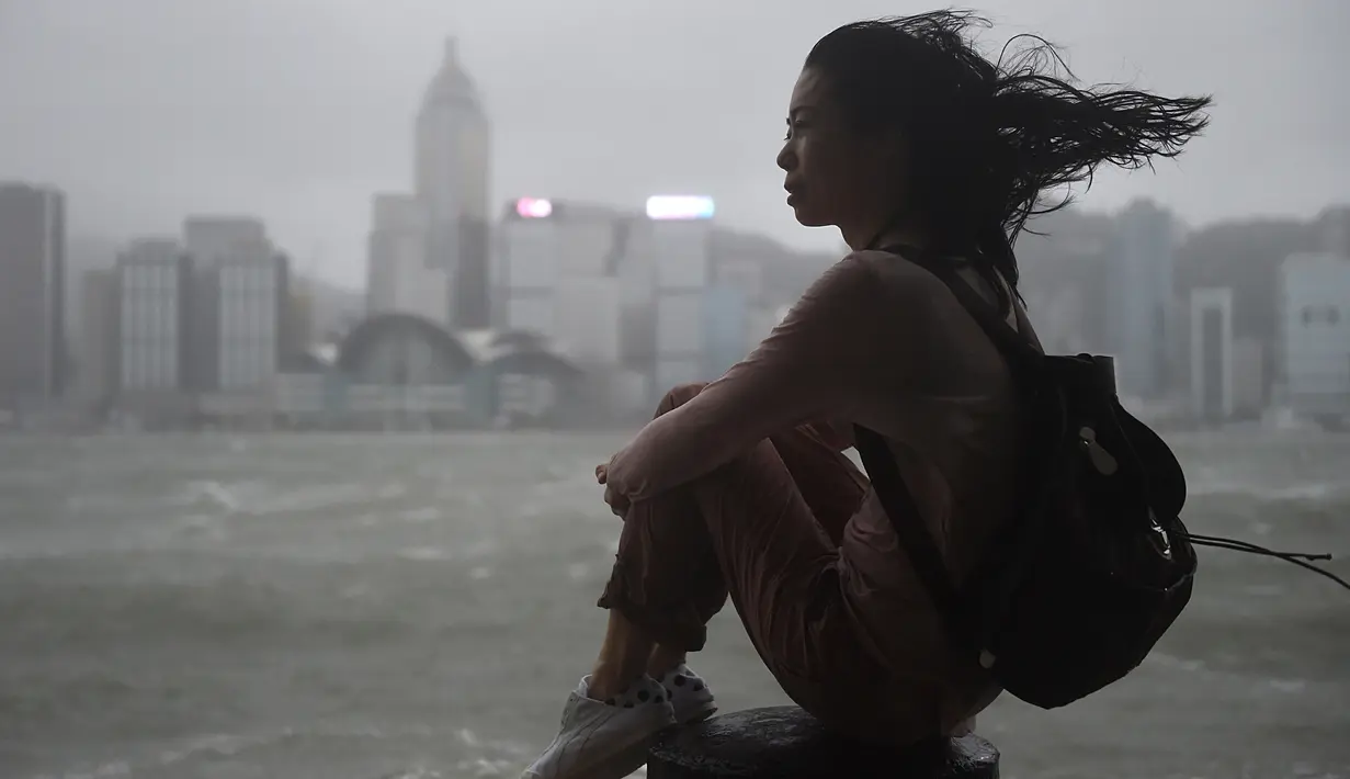 Seorang wanita melihat ke arah Victoria Harbour saat angin kencang dan hujan yang ditimbulkan oleh topan Hato di Hong Kong (23/8). Terjangan topan Hato mengakibatkan lebih dari 400 penerbangan dibatalkan. (AFP/Anthony Wallace)
