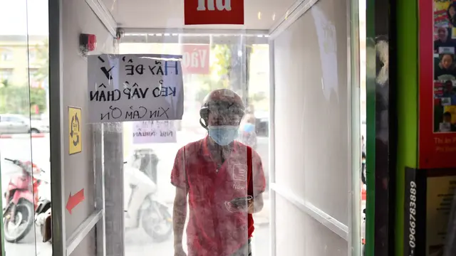 Seorang pengendara pengiriman makanan berjalan melalui mesin penyemprotan desinfektan di luar restoran Pizza. Di tengah pembatasan diberlakukan untuk membendung penyebaran Virus Corona COVID-19. (Manan Vatsyayana/AFP)