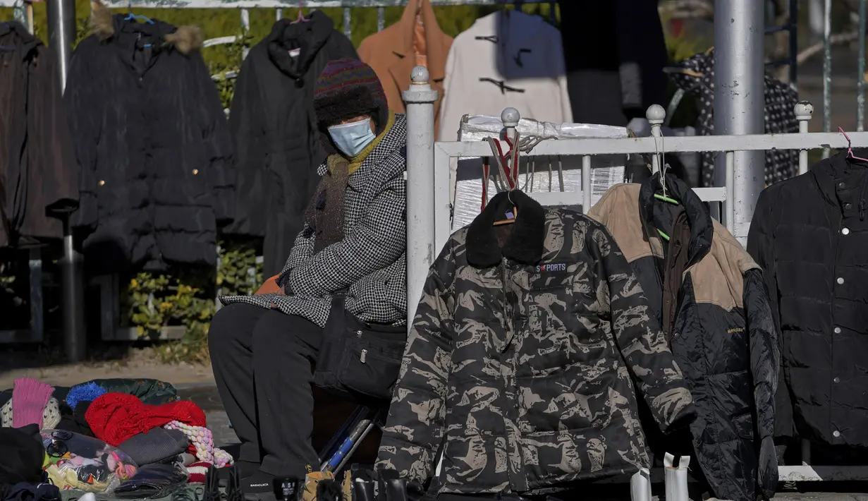 Seorang wanita yang mengenakan masker untuk membantu mengekang penyebaran virus corona mencoba menjual pakaian dan sepatu musim dingin di sebuah jalan di Beijing, Minggu (12/12/2021).  (AP Photo/Andy Wong)