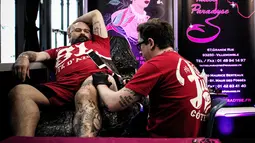 Seorang pria membuat tato di pahanya saat Paris Tattoo Convention di Grand Halle de la Villette, Paris, Prancis, Jumat (9/3). Paris Tattoo Convention tahun ini merupakan yang kedelapan. (Philippe LOPEZ/AFP)