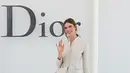 Karlie Kloss tampil ceria dengan blazer krem berkilau dipadukan rok tiered berlapis warna biru dusty yang playful. Ia tak ragu melambaikan tangan dengan tas mini krem [dok. Dior]