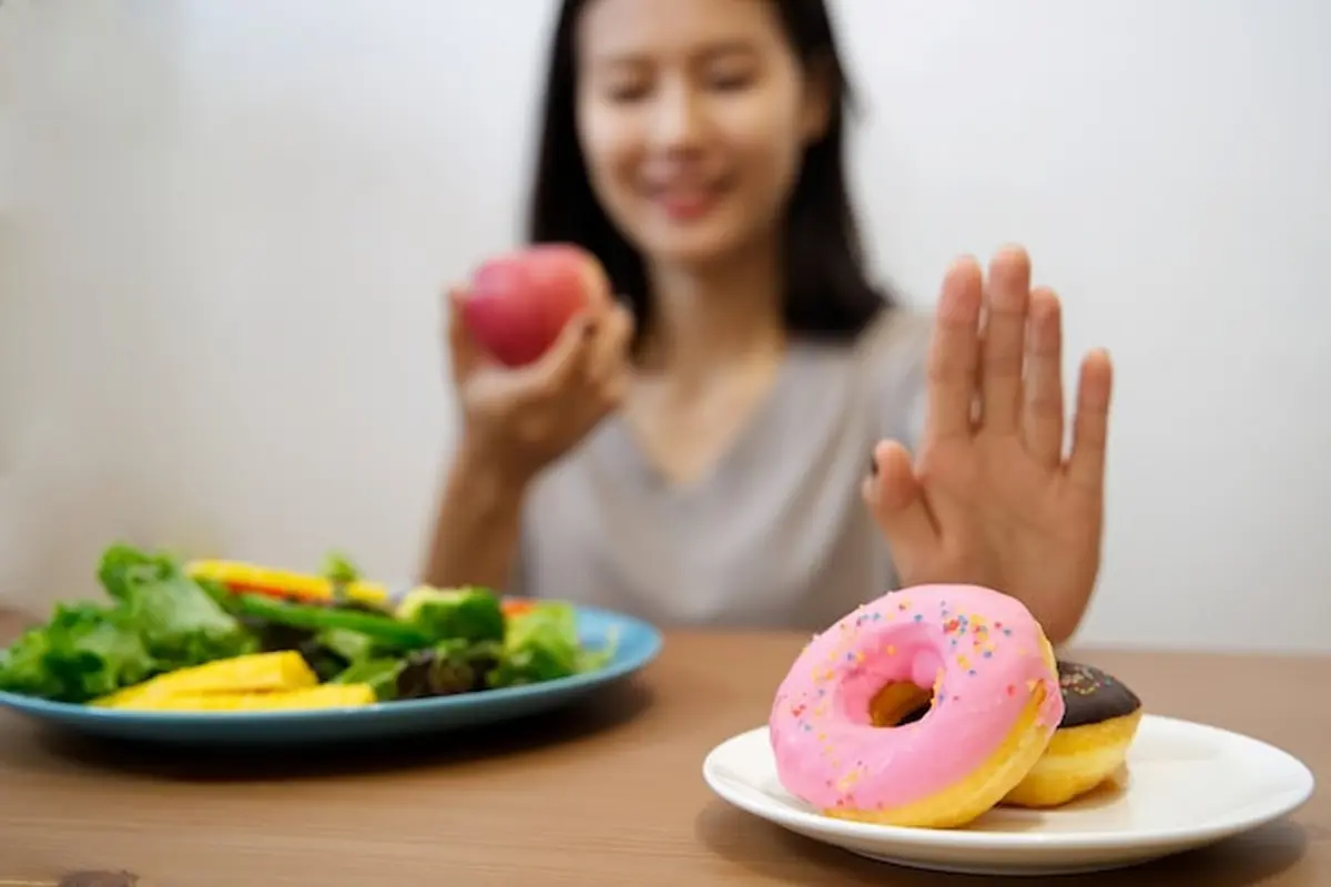 Seorang perempuan menolak sepiring donat dan hendak memakan buah serta sayuran (Foto Dok: Freepik/skawee)