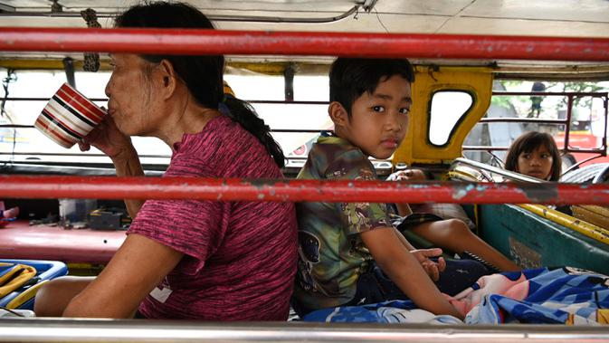 Seorang perempuan, Flores minum kopi di samping cucunya di dalam jeepney yang berfungsi sebagai rumah sementara di Manila, 12 Agustus 2020. Angkutan ikonik di Filipina itu belum dapat mengangkut penumpang sejak Maret akibat lockdown yang membuat jutaan orang kehilangan pekerjaan. (Ted ALJIBE/AFP)