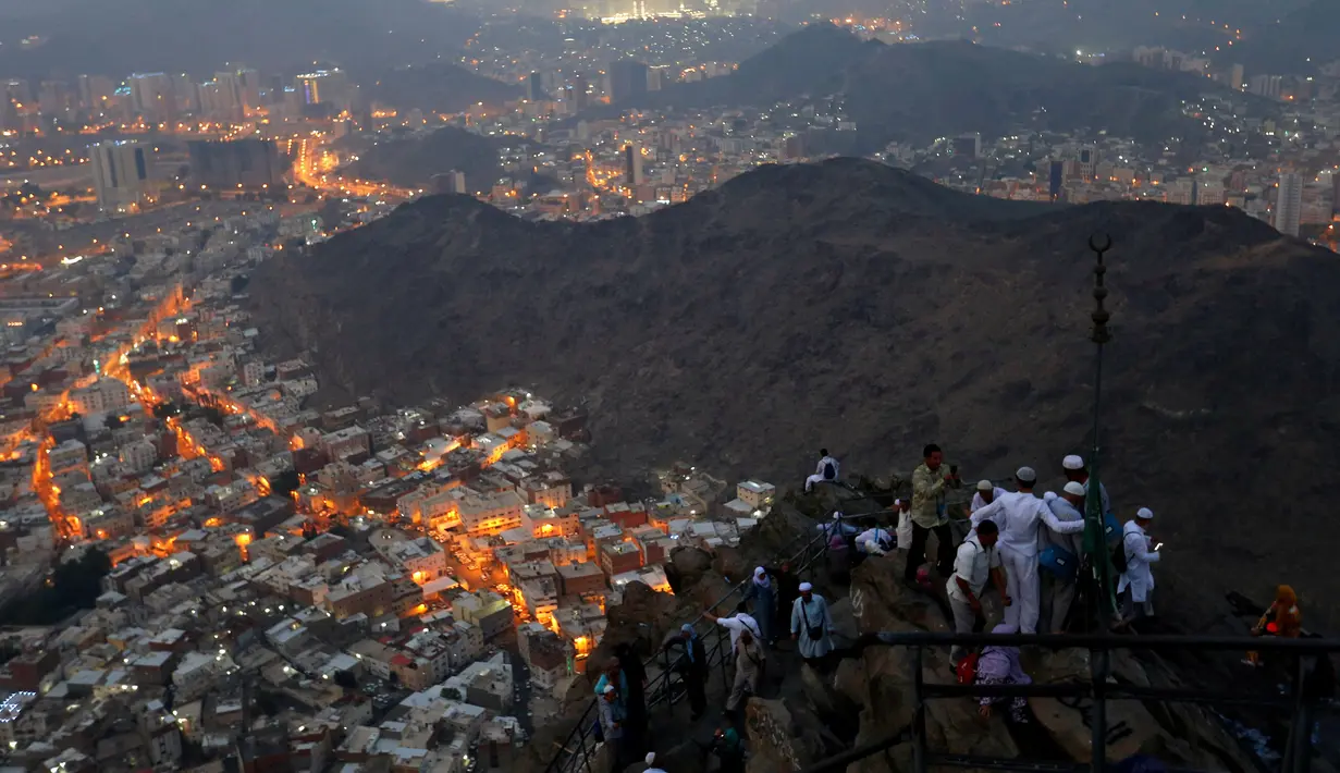 Para umat muslim berada di puncak Jabal Nur dengan pemandangan Kota Suci Mekah yang diterangi cahaya lampu saat malam hari ketika berziarah dan berdoa menjelang perayaan haji Idul Adha di Mekkah, Arab Saudi (7/9). (Reuters/Ahmed Jadallah)