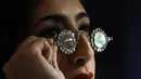 Seorang anggota staf mengenakan kacamata Mughal dengan lensa berlian, dalam bingkai berlian, di Sotheby's, di London, Jumat (22/10/2021). Dua pasang kacamata dari abad ke-17 ini akan dilelang 27 Oktober dengan perkiraan £1,5-2,5 Juta atau. (AP Photo/Alberto Pezzali)