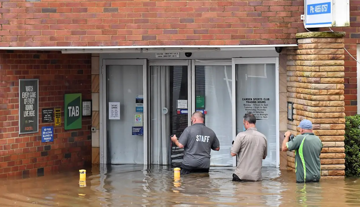 Staf Klub Olahraga Camden mengarungi banjir untuk masuk ke gedung di pinggiran barat daya Camden, Sydney, Australia, Selasa (8/3/2022). (Muhammad FAROOQ/AFP)