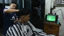Pelanggan tukang cukur asik menonton pertandingan Timnas Indonesia vs Australia pada babak 16 besar Piala Asia di kawasan Pinang, Tangerang, Minggu (28/1/2024). Indonesia tumbang empat gol tanpa balas. (Bola.com/M Iqbal Ichsan)