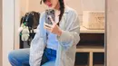 Ayu Ting Ting tampil kasual mengenakan tank top putih ditumpuknya dengan oversized shirt abu-abu, dan celana jeans panjang yang lebar, topi beige, sunglasses, dan sneakers yang berbeda warna antara kanan dan kiri. [Foto: Instagram/ayutingting92]