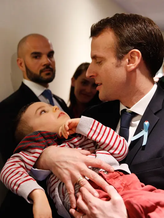 Presiden Prancis Emmanuel Macron menggendong seorang anak saat mengunjungi Graffiti's- Association Le Moulin Vert di Normandia, Prancis (5/4). Pada kunjungannya Presiden Emmanuel Macron berinteraksi dengan anak-anak autis.  (AP / Christophe Ena, Pool)