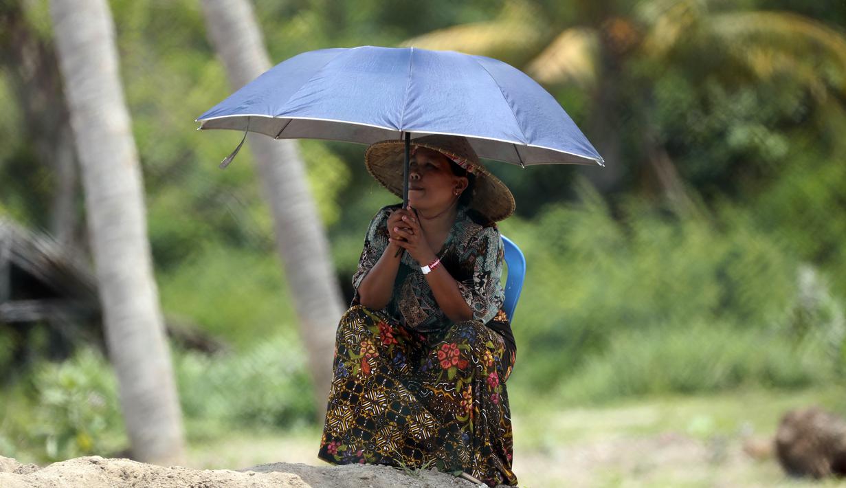Balapan terakhir Superbike musim ini juga dinikmati oleh seorang warga dengan menggunakan payung untuk menyaksikan latihan bebas World Superbike di luar Sirkuit Internasional Mandalika. (AP Photo/Achmad Ibrahim)