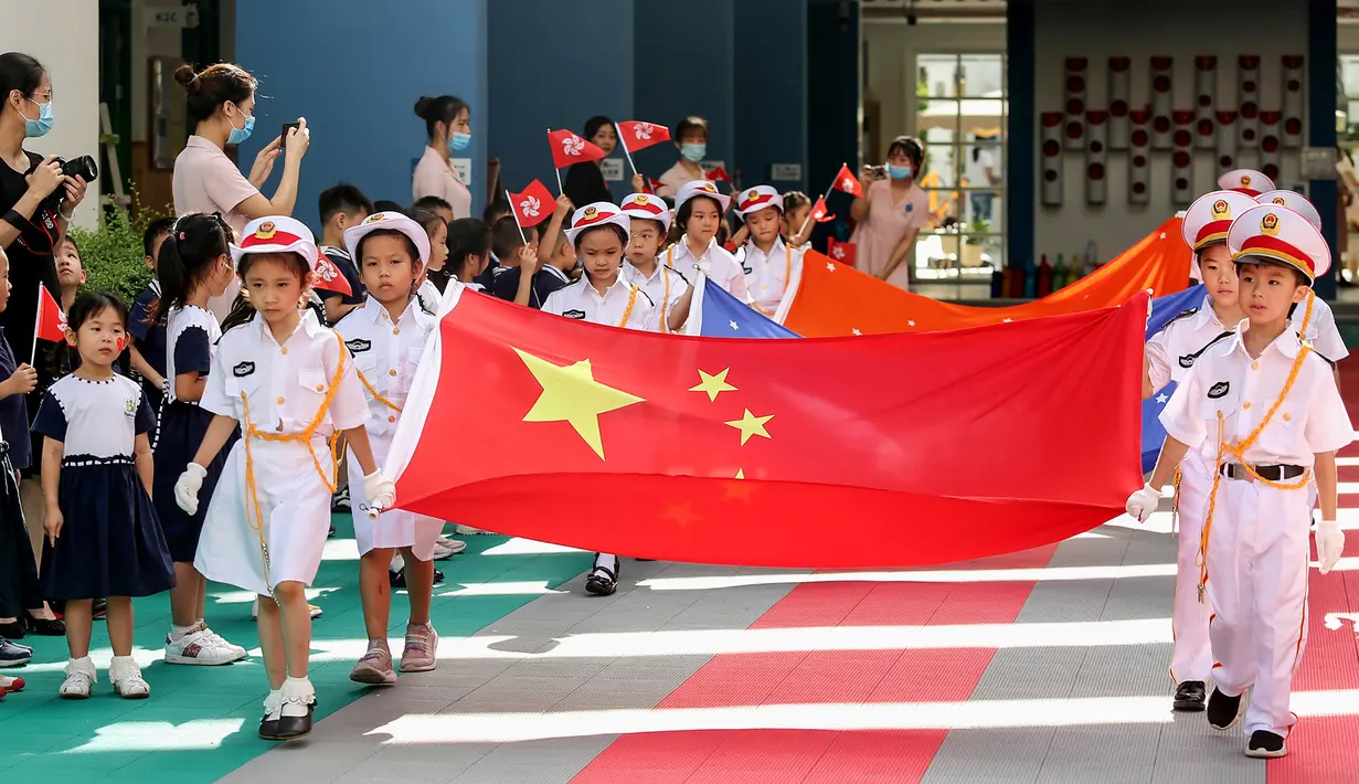 Anak-anak memegang bendera China saat upacara pengibaran bendera di sebuah taman kanak-kanak di Shenzhen, Provinsi Guangdong, China, Selasa (30/6/2020). Hong Kong menandai 23 tahun penyerahan dari Inggris ke Cina pada 1 Juli. (STR/AFP)