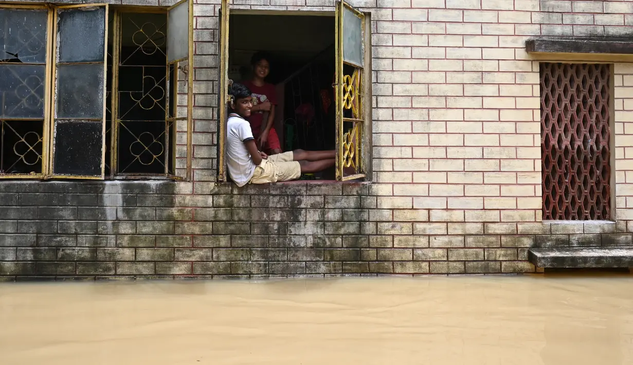 Warga duduk di jendela rumahnya ketika banjir merendam Ghatal, distrik Paschim Medinipur, sekitar 100 km dari Kolkata (2/8/2021). Perahu menjadi andalan warga untuk beraktivitas saat banjir. (AFP/Dibyangshu Sarkar)