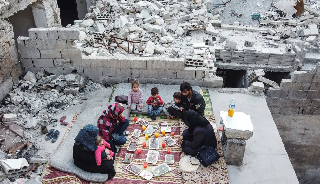 Keluarga Tareq Abu Ziad menunggu waktu berbuka puasa di tengah reruntuhan rumah mereka yang hancur setelah serangan militer pasukan pemerintah dan sekutunya di Kota Ariha, Provinsi Idlib, Suriah, Senin (4/5/2020). Muslim Suriah melewati Ramadan tahun ini masih dalam kondisi perang. (AAREF WATAD/AFP)