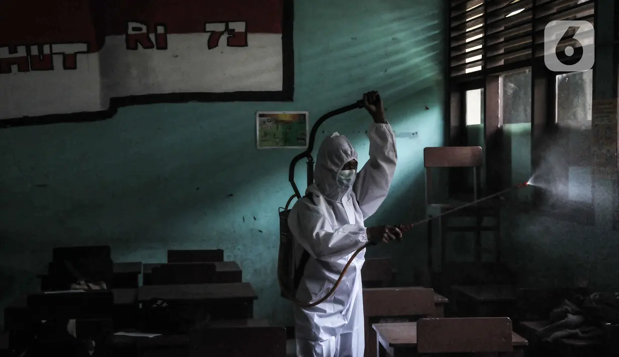 Petugas sekolah menyemprotkan disinfektan di ruang kelas usai Pembelajaran Tatap Muka (PTM) 100 persen di SMP Negeri 9 Depok, Senin (24/1/2022). Pihak sekolah melakukan penyemprotan disinfektan secara rutin seiring dimulainya pelaksanaan PTM 100 persen di Depok. (merdeka.com/Iqbal S Nugroho)