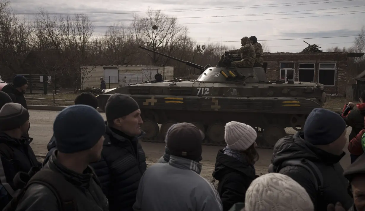 Warga yang mengantre bantuan menyaksikan tentara Ukraina menaiki tank di kota Trostsyanets, Ukraina, Senin, 28 Maret 2022. Trostsyanets baru-baru ini direbut kembali oleh pasukan Ukraina setelah dikuasai oleh Rusia sejak awal perang. (AP Photo/Felipe Dana)
