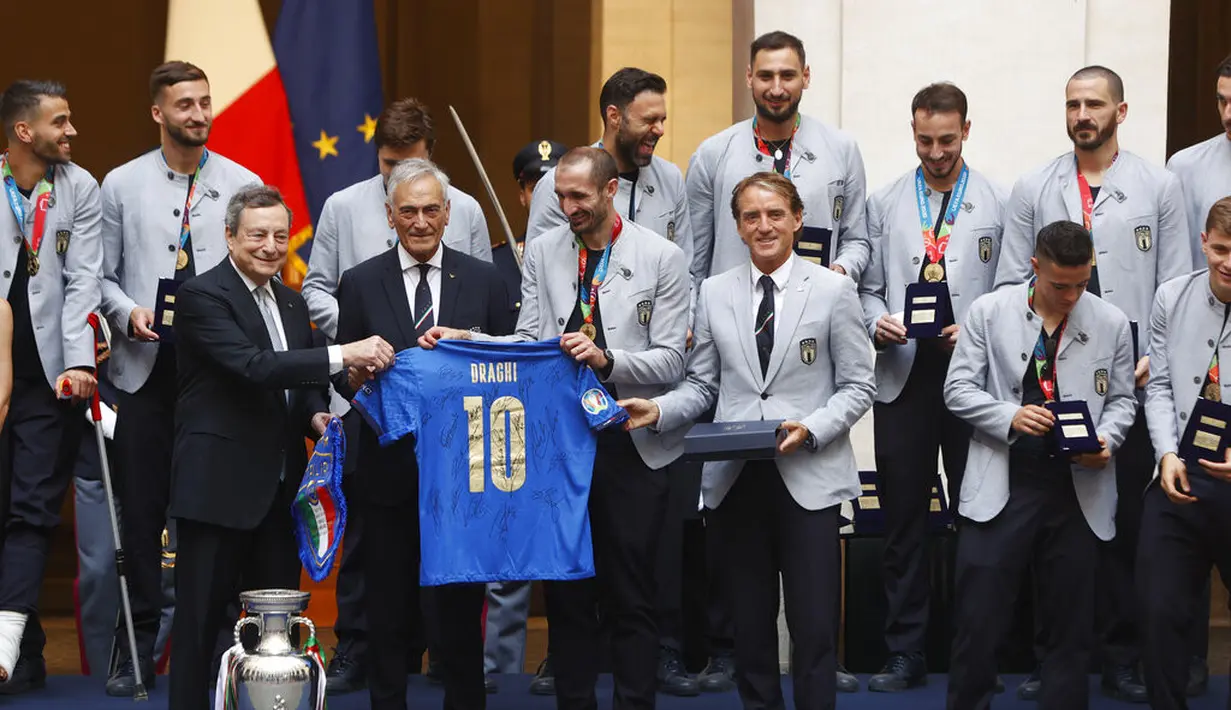 Perdana Menteri Italia Mario Draghi menerima jersey Italia dengan namanya dari Presiden Federasi Sepak Bola Italia Gabriele Gravina dan para pemain dan pelatih Roberto Mancini dalam sebuah upacara perayaan juara Euro 2020 di Istana Chigi di Roma, Senin (12/7/2021). (AP Photo/Riccardo De Luca)