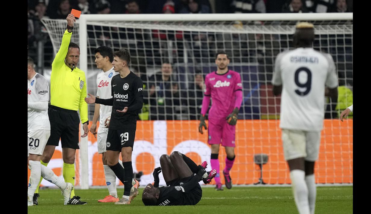 <p>Pemain Eintracht Frankfurt, Randal Kolo Muani (tengah) mendapatkan kartu merah dari wasit Artur Dias pada laga leg pertama 16 besar Liga Champions 2022/2023 melawan Napoli yang berlangsung di Deutsche Bank Park, Rabu (22/2/2023) WIB. (AP Photo/Michael Probst)</p>