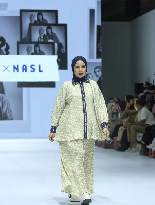 Tya Ariestya tampil percaya diri sebagai muse dalam kolaborasi ini, mengenakan kerudung navy blue yang dipadukan dengan kemeja bermotif pleated hijau yang dihiasi list kerang, lengan, dan kancing berwarna biru. Kemeja tersebut selaras dengan celana flare pleated yang dikenakannya. [Dok/Fimela/Adrian Utama P].