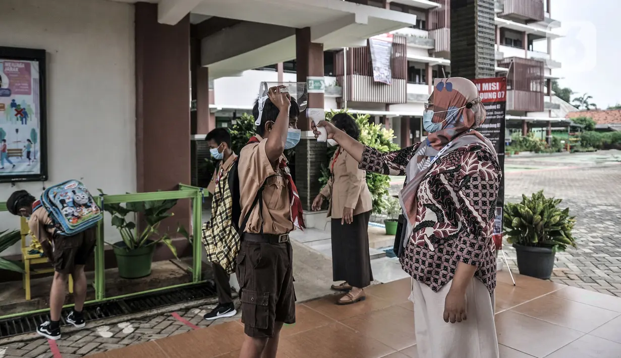 Tim Satgas COVID-19 bentukan pihak sekolah memeriksa suhu tubuh siswa saat hari pertama uji coba pembelajaran tatap muka di SDN Pulogadung 07, Jakarta, Rabu (7/4/2021). Pembelajaran tatap muka dilakukan dengan menerapkan protokol kesehatan yang ketat. (merdeka.com/Iqbal S. Nugroho)