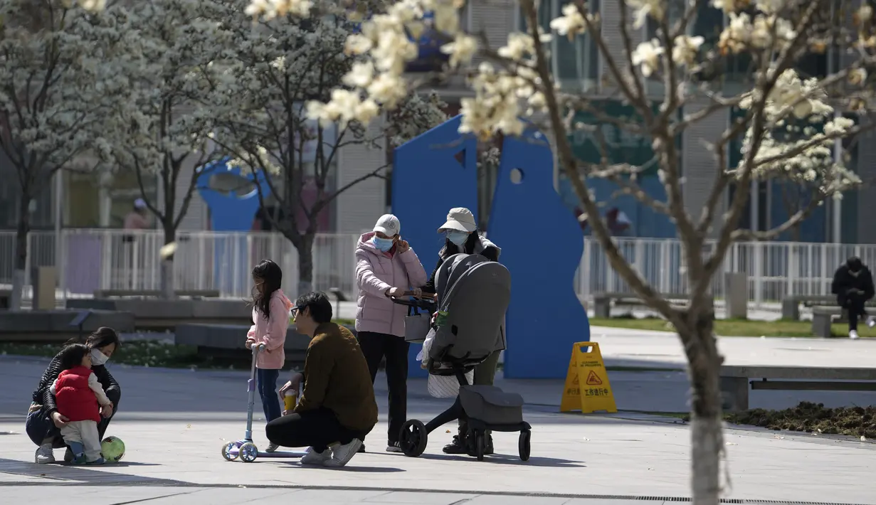 Warga yang mengenakan masker membawa anak-anak mereka berjemur di luar kompleks perumahan di Beijing, Minggu (3/4/2022). Kasus COVID-19 di kota terbesar di China, Shanghai, masih meningkat saat jutaan orang tetap terisolasi di rumah di bawah lockdown besar-besaran. (AP Photo/Andy Wong)