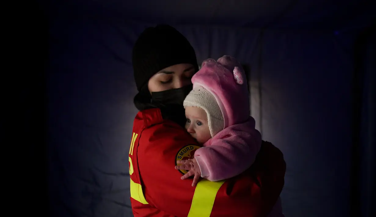 Seorang pekerja dari Inspektorat Situasi Darurat menenangkan bayi yang menangis dari sebuah keluarga yang melarikan diri dari konflik dari negara tetangga Ukraina di perbatasan Rumania-Ukraina, di Siret, Rumania, Sabtu, 26 Februari 2022. (AP Photo/Andreea Alexandru)