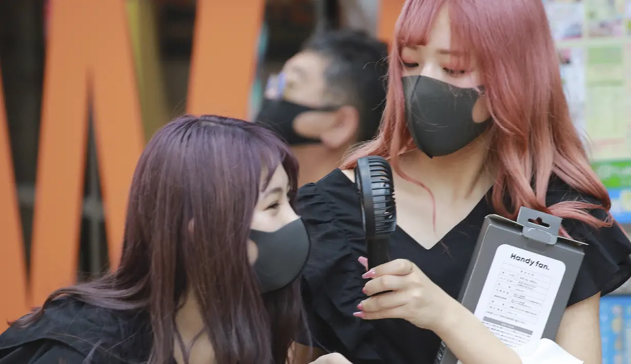 Sejumlah memakai masker wajah untuk membantu melindungi dari penyebaran coronavirus memegang kipas angin portabel untuk menghindari panas di Tokyo, Rabu, (5/8/2020). (AP Photo/Koji Sasahara)