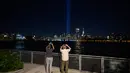 Orang-orang mengambil foto dari instalasi 'Tribute in Light' di tepi perairan Brooklyn untuk memperingati serangan teroris 9/11, di New York (10/9/2021). (AFP/Ed Jones)