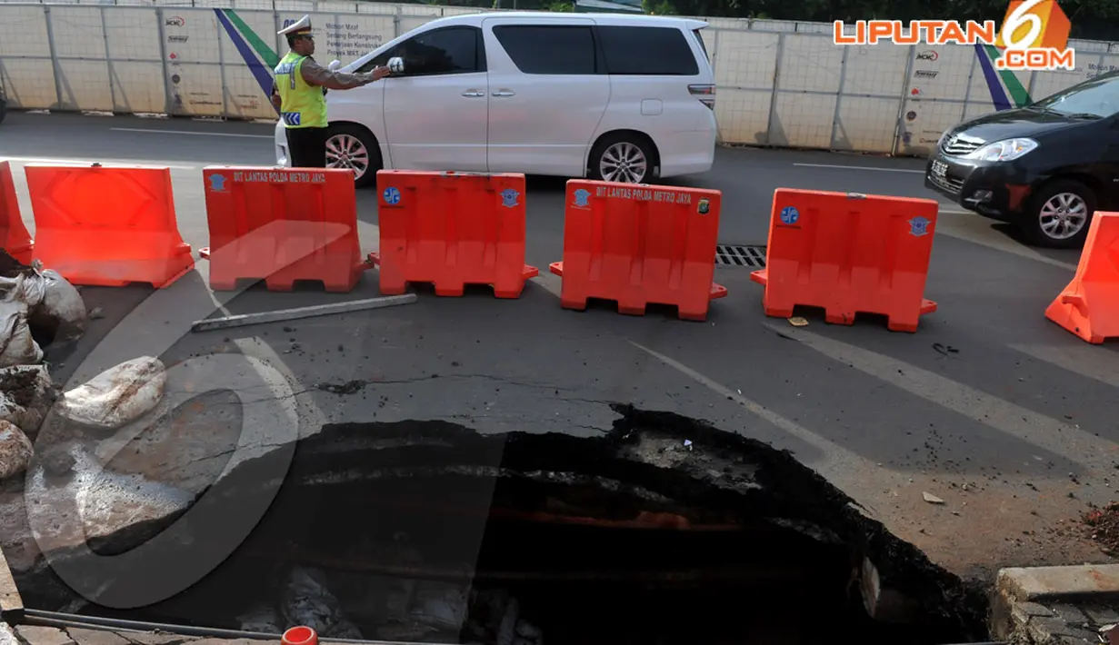 Seorang Polisi tampak mengatur lalu lintas agar tak macet di sekitar jalan yang amblas di kawasan Sudirman . Kamis (10/4/2014)  (Liputan6.com/Johan Tallo).