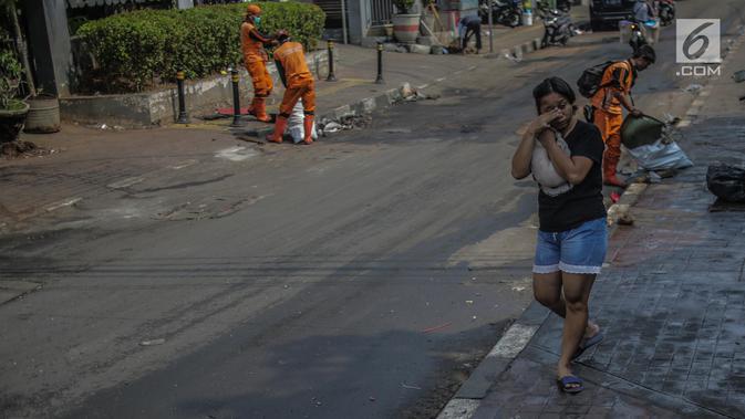 Warga menutupi matanya untuk menghindari sisa gas air mata pasca bentrok massa dengan aparat di Palmerah, Jakarta, Kamis (26/9/2019). Banyak masyarakat yang melintas dan warga sekitar perih pada mata hingga bersin akibat sisa gas air mata pasca bentrokan kemarin. (Liputan6.com/Faizal Fanani)