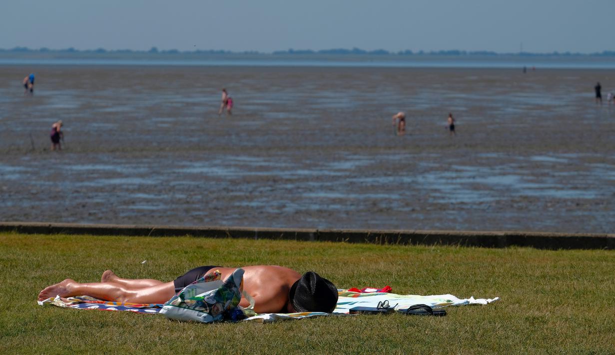 Seorang pria berjemur saat suhu mencapai 34 derajat Celcius di dekat pantai Laut Utara di Wremen, Jerman barat (24/7/2019). Peramal cuaca memprediksi suhu tertinggi di seluruh Eropa barat yang terkena gelombang panas akan mencetak rekor suhu terbaru.  (AFP Photo/Patrik Stollarz)