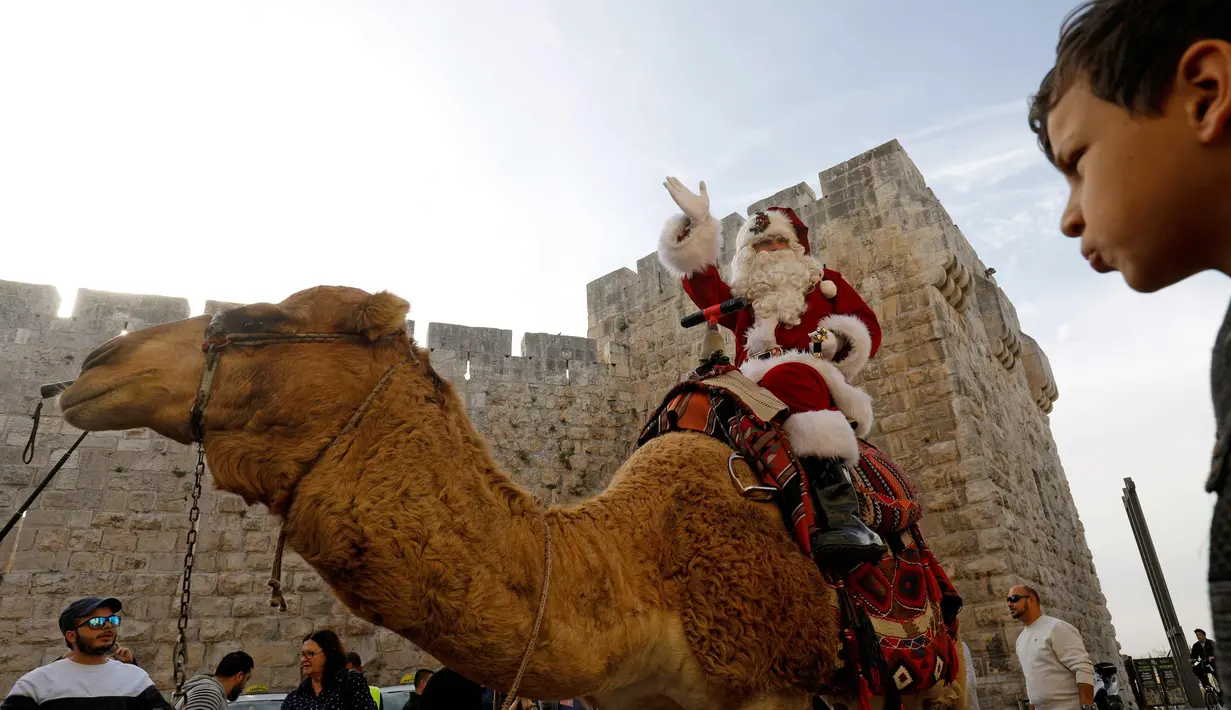 Warga melihat seorang pria mengenakan busana seperti Santa Claus mengendarai unta menyambut perayaan Natal di sepanjang tembok Ottoman Kota Tua Yerusalem (21/12). (AFP Photo/Gali Tibbon)