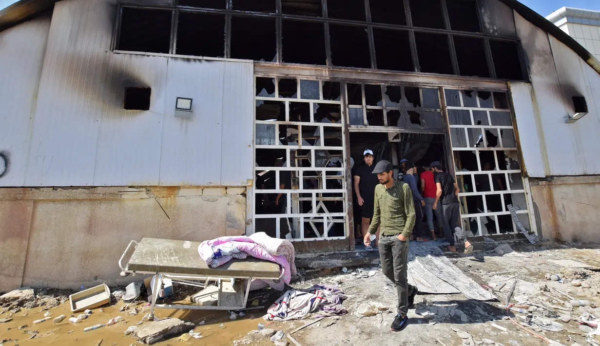 Orang-orang melihat bangsal isolasi corona COVID-19 yang rusak di rumah sakit Al-Hussein setelah kebakaran besar di kota Nasiriyah, Selasa (13/7/2021). Selain dihadapi oleh perang dan sanksi, Irak juga berusaha bertahan dengan sistem medisnya dalam mengatasi krisis Virus Corona. (Asaad NIAZI/AFP)