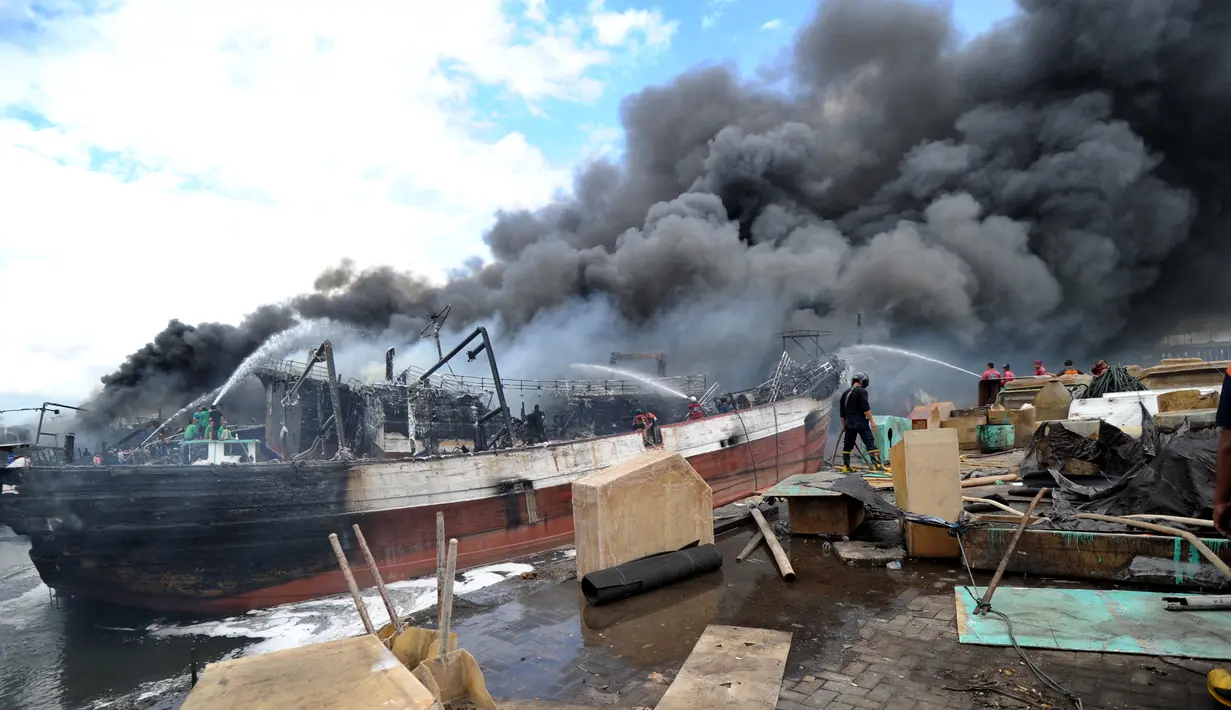 Petugas pemadam kebakaran dibantu pekerja mencoba memadamkan api di kapal nelayan di Pelabuhan Benoa, Denpasar, Bali, Senin (9/7). Upaya pemadaman melibatkan 11 unit mobil pemadam kebakaran. (SONNY TUMBELAKA/AFP)
