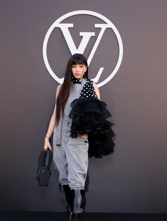 Hyein NewJeans bergaya industrial kenakan jumpsuit abu-abu dengan boots kulit. Sentuhan scarf polkadot dengan tiered ruffles jadi aksen playful [LouisVuitton]