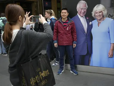 Seorang turis berpose di samping potret besar Raja Charles III dan Ratu Camilla  yang dipajang di Stasiun Kings Cross di London, Senin, 1 Mei 2023. Penobatan Raja Charles III akan berlangsung di Westminster Abbey pada 6 Mei. (AP Photo/Kirsty Wigglesworth)