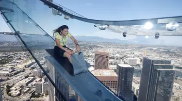 Seorang wanita mencoba berseluncur menggunakan skyslide di lantai 69 dan 70 dari Bank Tower AS, Los Angeles , California, (20/6). Tempat yang dinamakan OUE Skyspace LA ini kita dapat melihat panorama indah kota LA dari atas. (REUTERS / Lucy Nicholson)