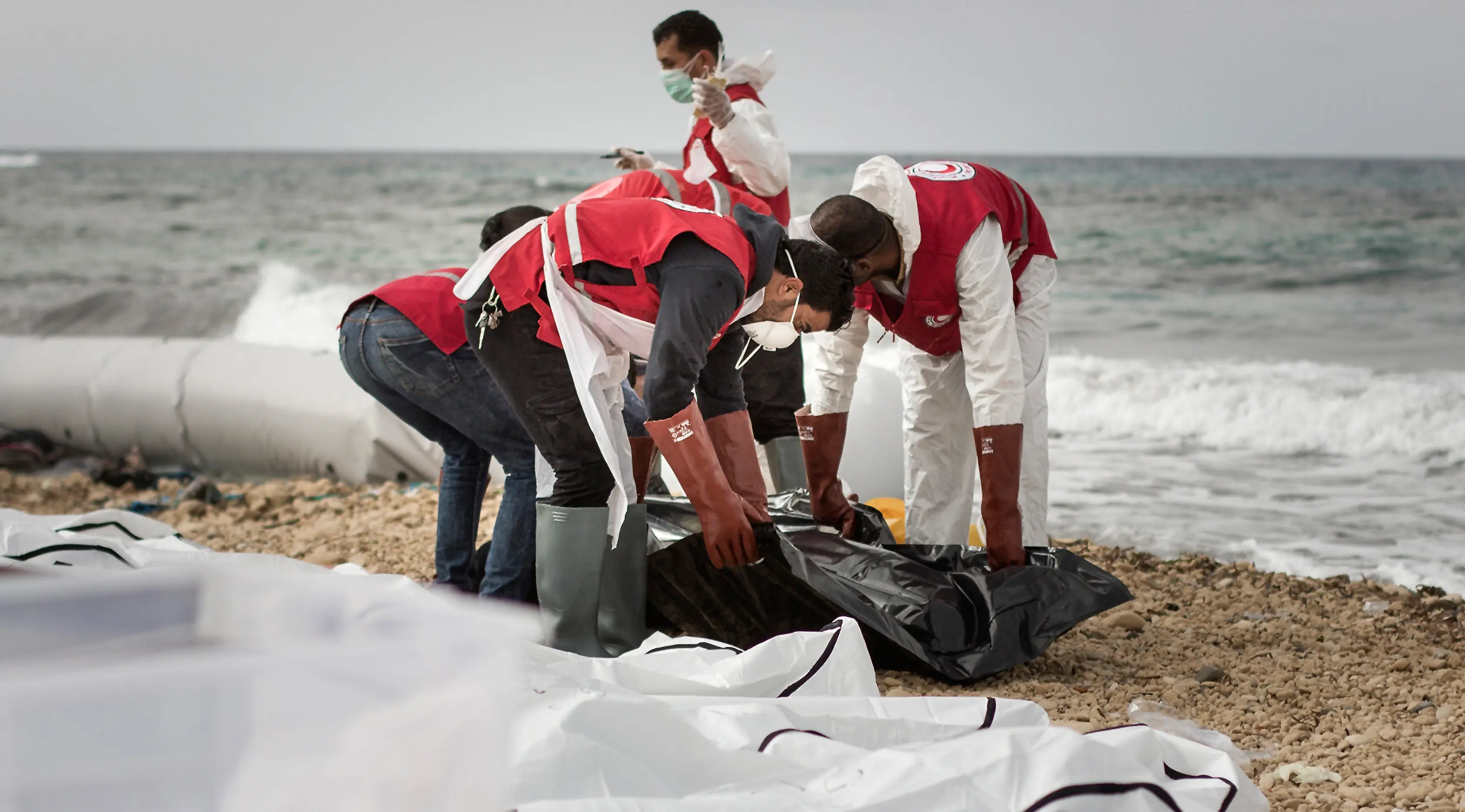 Petugas Bulan Sabit Merah Libya mengumpulkan jenazah para imigran yang ditemukan terdampar di pantai utara Libya, Selasa (21/2). Sedikitnya 74 jenazah imigran tenggelam saat melintasi perairan Mediterania dalam upaya mencapai Eropa. (AMIN ELAMR/AFP)