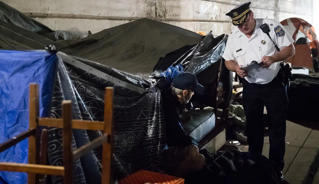 Seorang petugas polisi mengusir seorang pria yang tinggal dalam tendanya di bawah jembatan di Philadelphia (30/5). Selain itu tempat yang mereka tinggali menjadikan bagian kota terlihat kotor dan kumuh. (AP Photo/Matt Rourke)