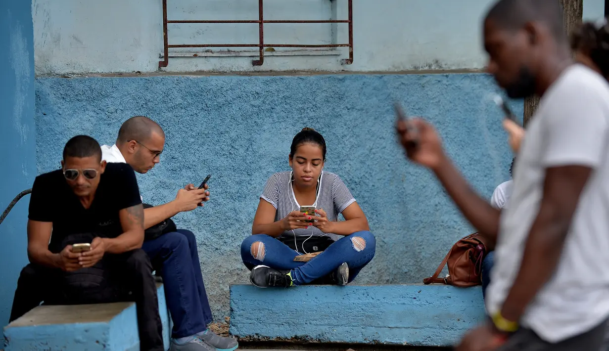 Orang-orang menggunakan ponsel mereka untuk terhubung ke internet melalui WiFi di sebuah taman di Havana, Rabu (5/12). Pemerintah Kuba mengumumkan bahwa masyarakat bisa mengakses internet secara bebas di ponsel mereka mulai Kamis ini. (YAMIL LAGE/AFP)