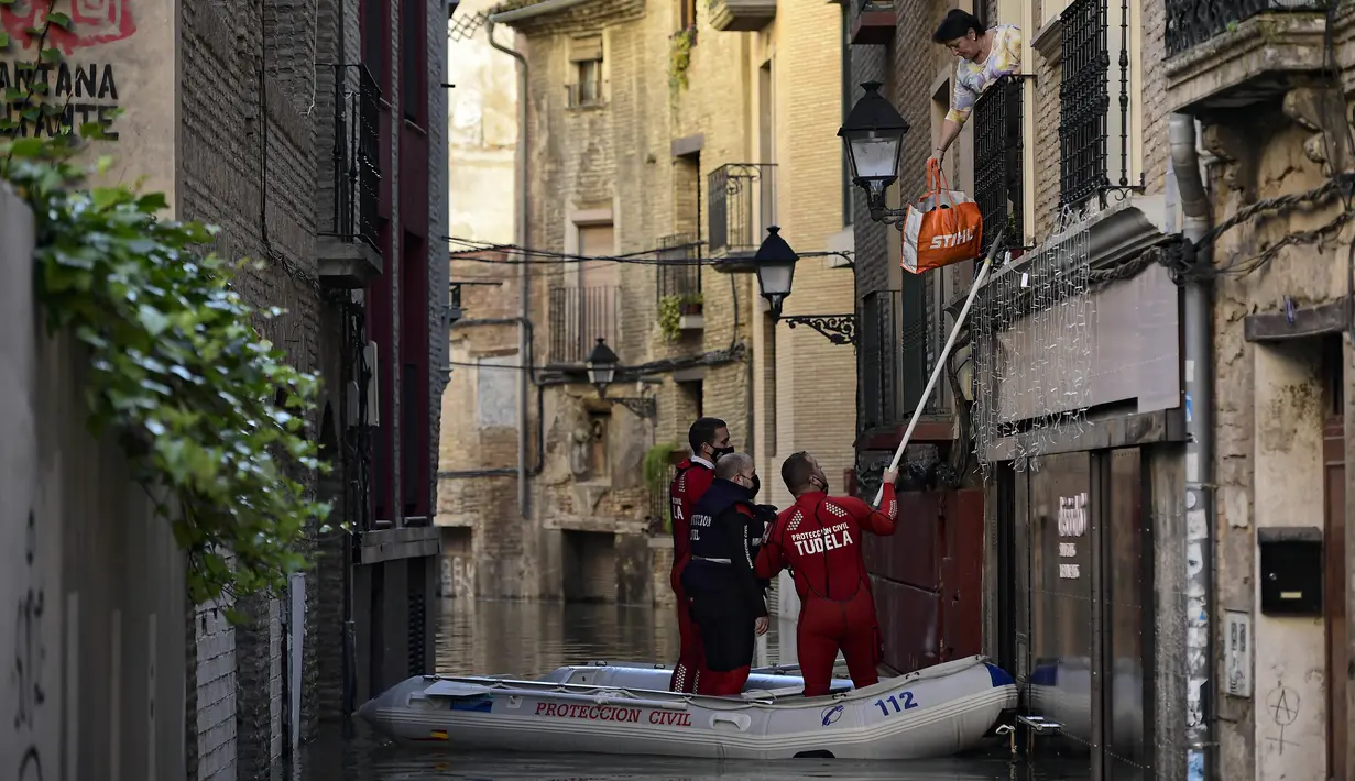 Tim penyelamat membantu seorang wanita di rumahnya di daerah banjir dekat Sungai Ebro di Tudela, Spanyol utara (12/12/2021). Hujan deras menyebabkan banjir di Spanyol utara. (AP Photo/Alvaro Barrientos)
