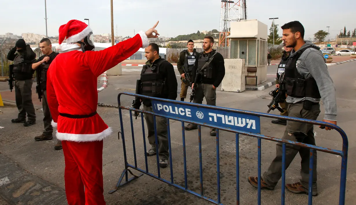 Pengunjuk rasa berkostum Santa Claus berhadapan dengan petugas penjaga perbatasan saat aksi di desa Tepi Barat Bilin dekat Ramallah, Jumat (23/12). Pengunjuk rasa menentang pembangunan tembok pembatas di Israel. (REUTERS/Mussa Issa Qawasma)