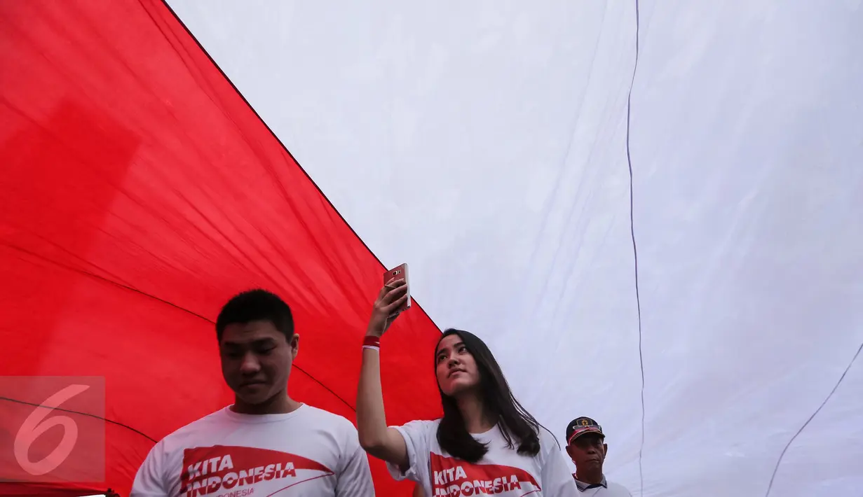 Peserta 'Aksi Kita Indonesia' berjalan di bawah Bendera Merah Putih raksasa yang dibawa berkeliling Bundaran HI, Jakarta, Minggu (4/12). Aksi Kita Indonesia atau Aksi 412 diinisiasi oleh partai-partai pendukung Pemerintah. (Liputan6.com/Fery Pradolo)