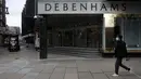 Seorang pria yang mengenakan masker berjalan melewati papan informasi virus corona di sebelah department store andalan Debenhams yang ditutup di Oxford Street di London, Sabtu (6/2/2021). Debenhams, yang berusia 242 tahun, menyatakan mereka dalam proses penutupan massal. (AP Photo/Matt Dunham)